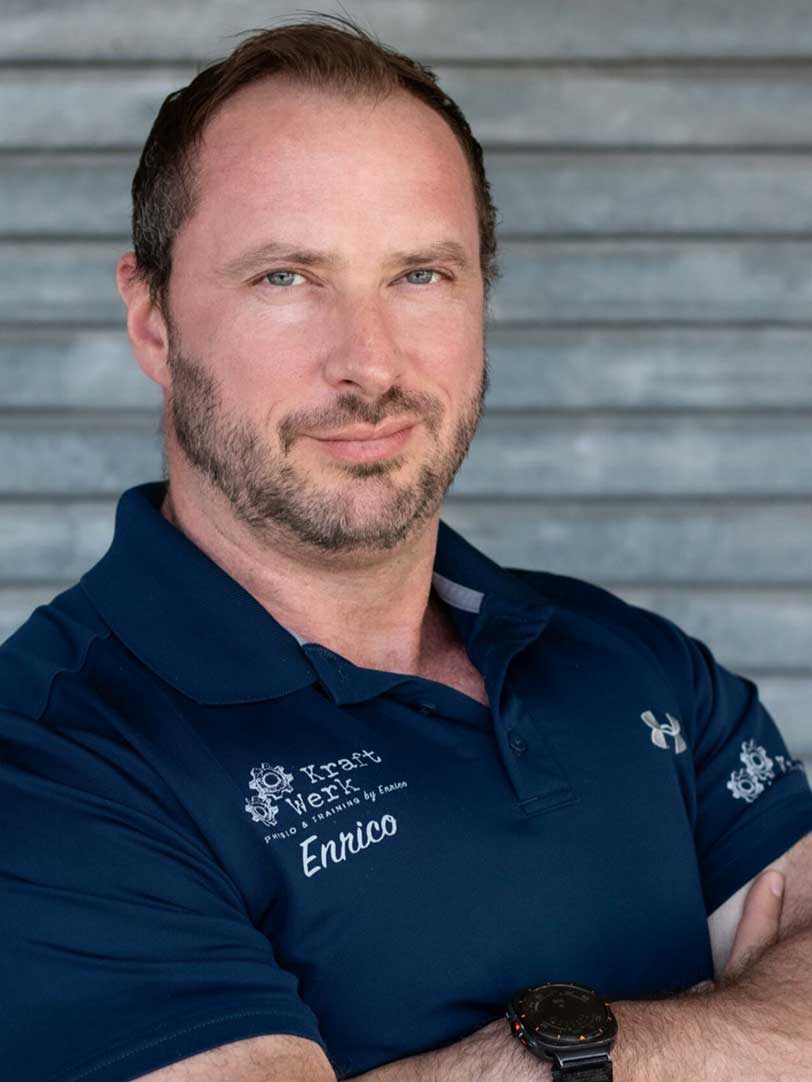 Ein Mann mit Bart in einem blauen Poloshirt lächelt selbstbewusst vor grauen Streifen.