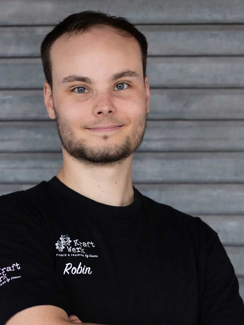 Mann mit Bart und kurzen Haaren lächelt in schwarze Kleidung vor grauem Hintergrund