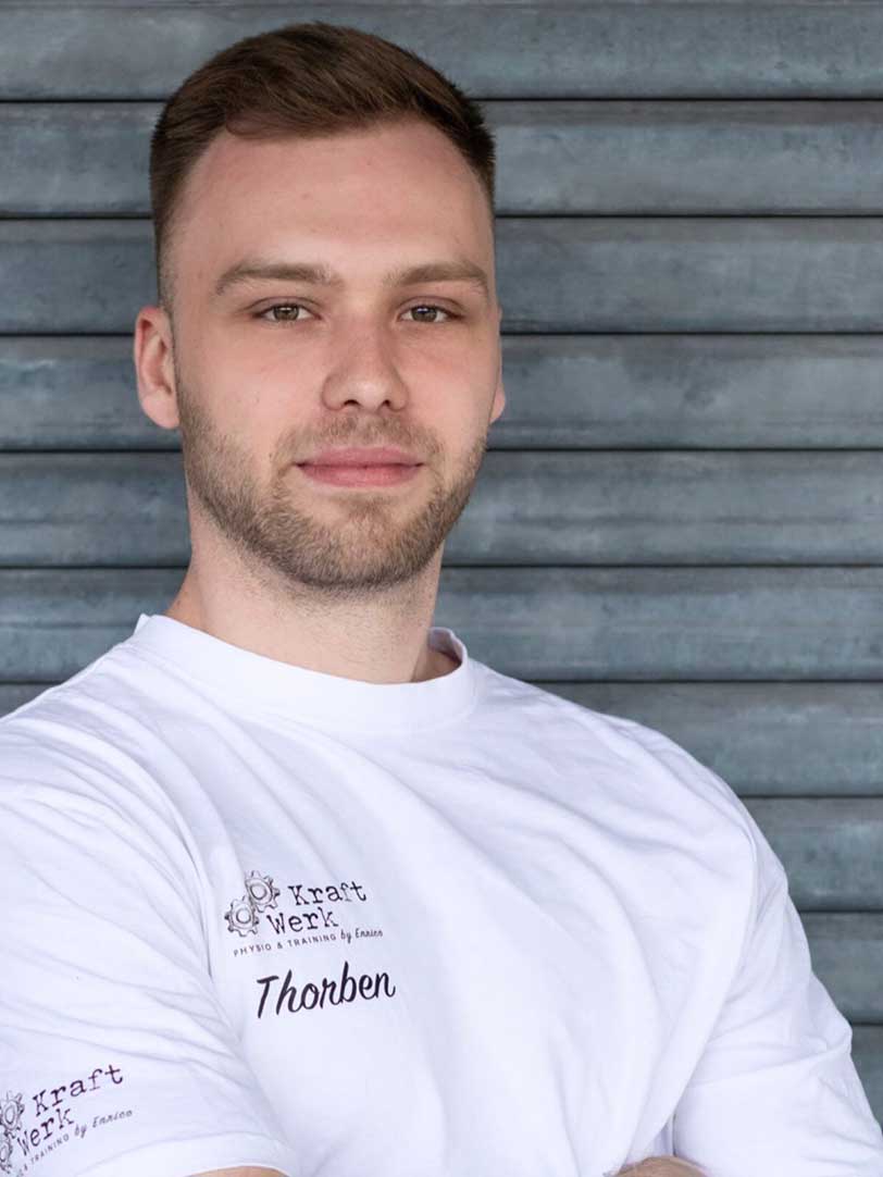 Mann mit kurzem Haar, lächelnd, im weißen T-Shirt vor grauer Wand stehend